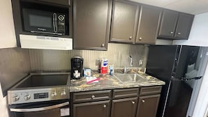 A compact kitchen with dark cabinets, a microwave, a stove, a sink, and a refrigerator. - BOARDWALK BLISS/GREAT LOCATION (Myrtle Beach)