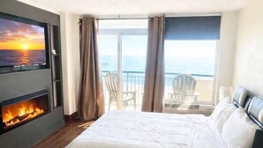 A hotel room with a large bed, a fireplace, a TV mounted on the wall, and a balcony with a view of the sea. - BOARDWALK BLISS/GREAT LOCATION (Myrtle Beach)