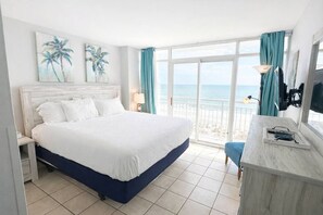 Habitación de hotel con una cama grande, un escritorio con lámpara y vista a la playa.