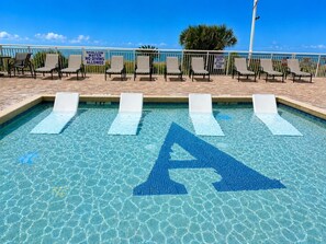 Ein flaches Schwimmbecken mit Sprungbrett, Liegestühlen und blauem Himmel.