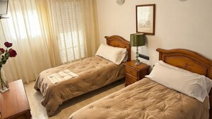 Een hotelkamer met twee bedden, een nachtkastje met een lamp, een lijst met een afbeelding aan de muur, en een vaas met bloemen op een nachtkastje.