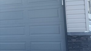 A garage door with a stone base and a light-colored siding wall. - New basement suite in a beautiful & nice location (Winnipeg)