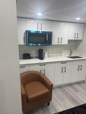 A modern kitchen with white cabinets, a stainless steel microwave, a coffee maker, and a sink. - New basement suite in a beautiful & nice location (Winnipeg)