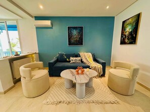 A living room with a dark blue wall, a sofa, two armchairs, a coffee table, and a painting. - Les Suites Jumelles Sea View Gammarth (La Marsa)