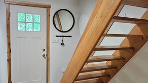 Een kamer met een houten trap, een witte deur met een raam, en een spiegel aan de muur.