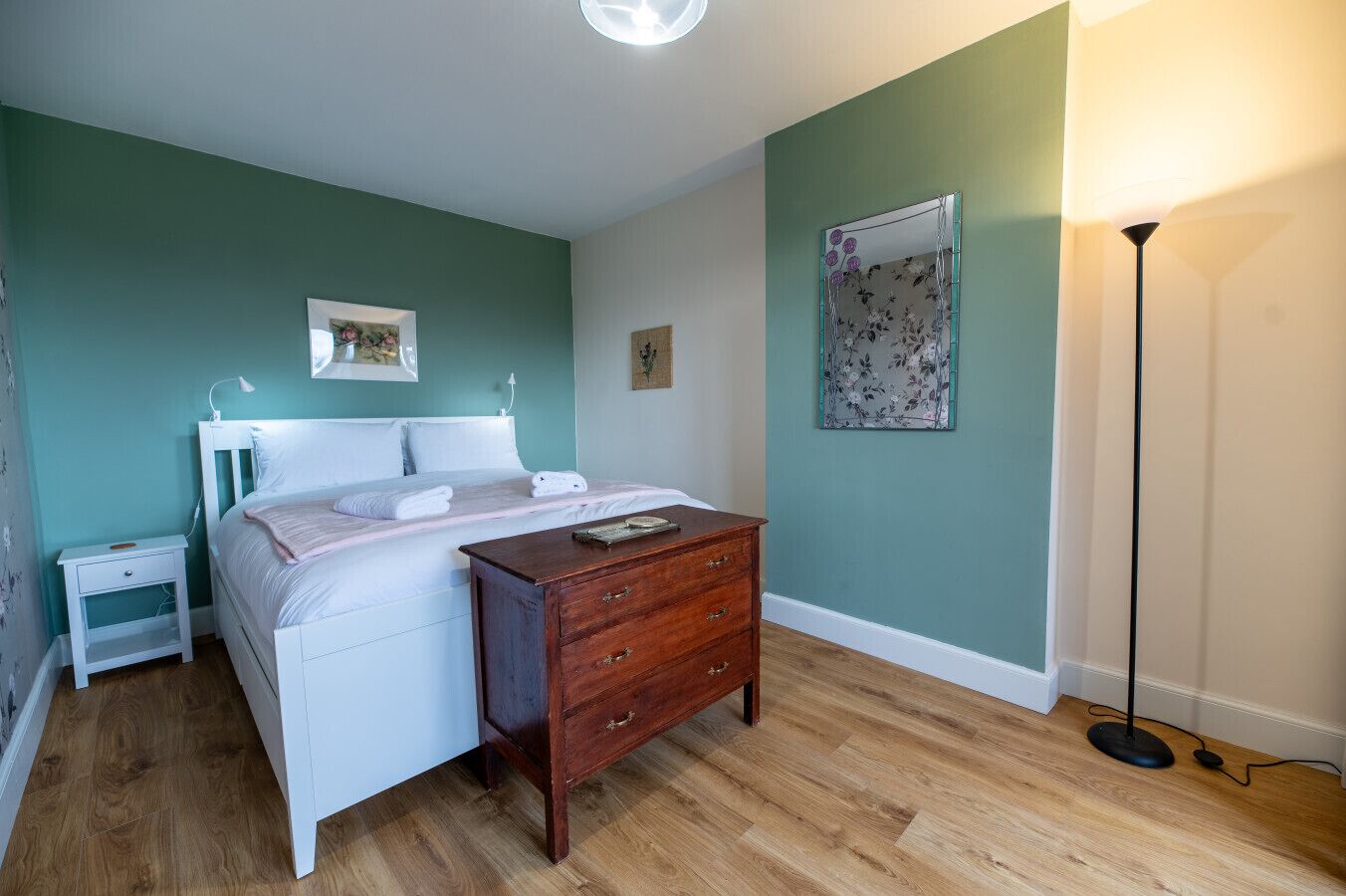 Un dormitorio con cama, mesita de noche, cómoda y lámpara de pie.