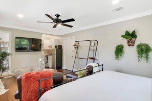 A bedroom with a bed, a ceiling fan, a TV, and a kitchenette in the background. - New Studio Apartment w/ Kitchen - A (West Palm Beach)