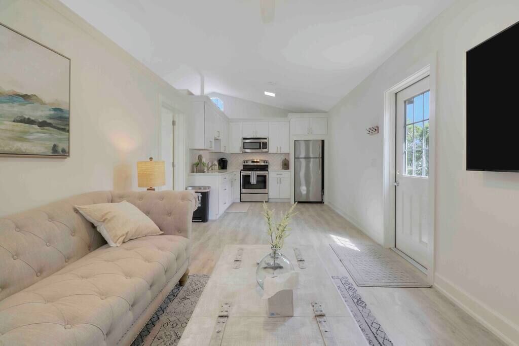 A spacious living area with a beige sofa, a coffee table with a vase, and a kitchen in the background.