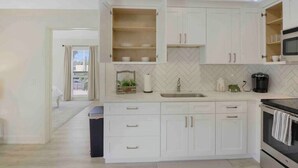 Une cuisine moderne avec des meubles blancs, un dosseret en carreaux disposés en chevron et un micro-ondes encastré.