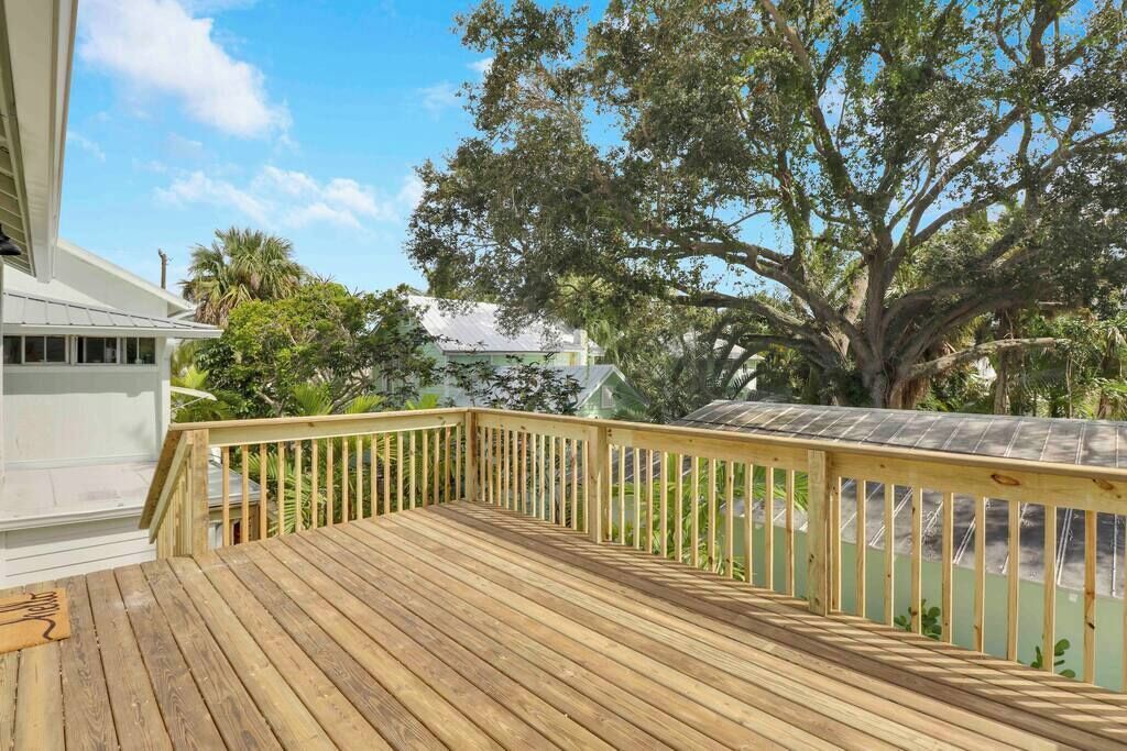 Una terraza de madera con barandilla, rodeada de follaje y un árbol grande.