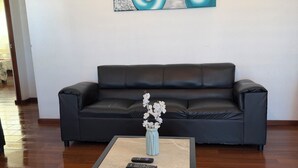 Una sala de estar con un sofá de cuero negro, una mesa de centro con un florero de flores blancas y un cuadro abstracto colgado en la pared.
