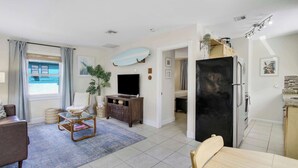 A modern living room with a sofa, a coffee table, a TV, and a dining area with a table and chairs. - Cottage 3 on Penn - Pool! (West Palm Beach)