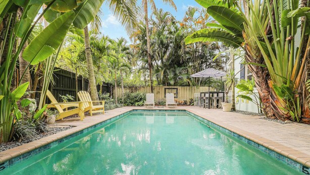 A rectangular swimming pool surrounded by lush tropical plants and a wooden fence. - Cottage 3 on Penn - Pool! (West Palm Beach)