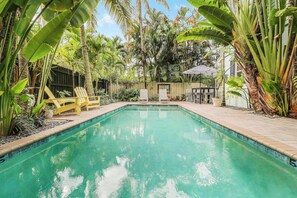 A rectangular swimming pool surrounded by lush tropical plants and a wooden fence. - Cottage 3 on Penn - Pool! (West Palm Beach)