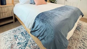 Een slaapkamer met een bed, nachtkastjes, een plafondventilator, wanddecoratie en een deur.