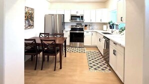 Een moderne keuken met witte kasten, roestvrijstalen apparatuur en een eethoek met houten stoelen.