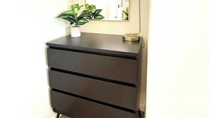 Een hoekje met een zwarte dressoir, een spiegel en een potplant.