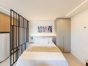 Moderni hotellihuone, jossa on sänky, vaatekaappi ja yöpöytä.