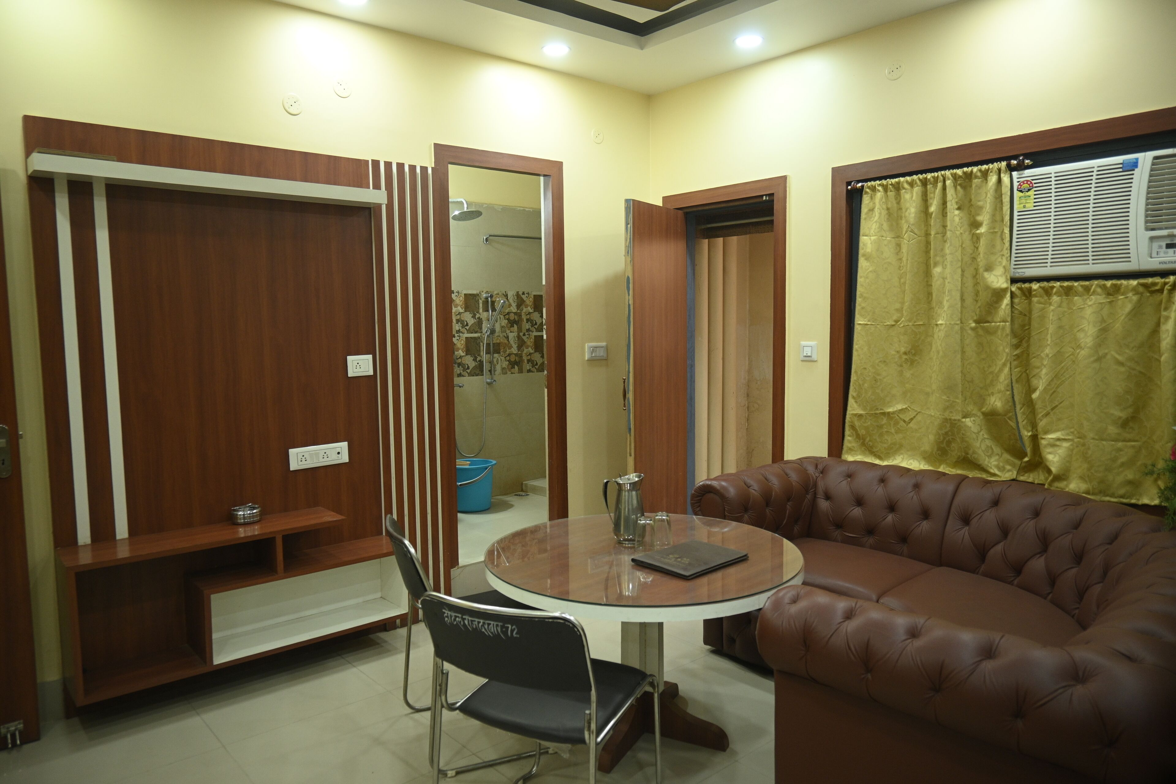Un espace de vie compact comprenant une table ronde, un canapé en cuir marron, une armoire avec un miroir et un seau bleu.