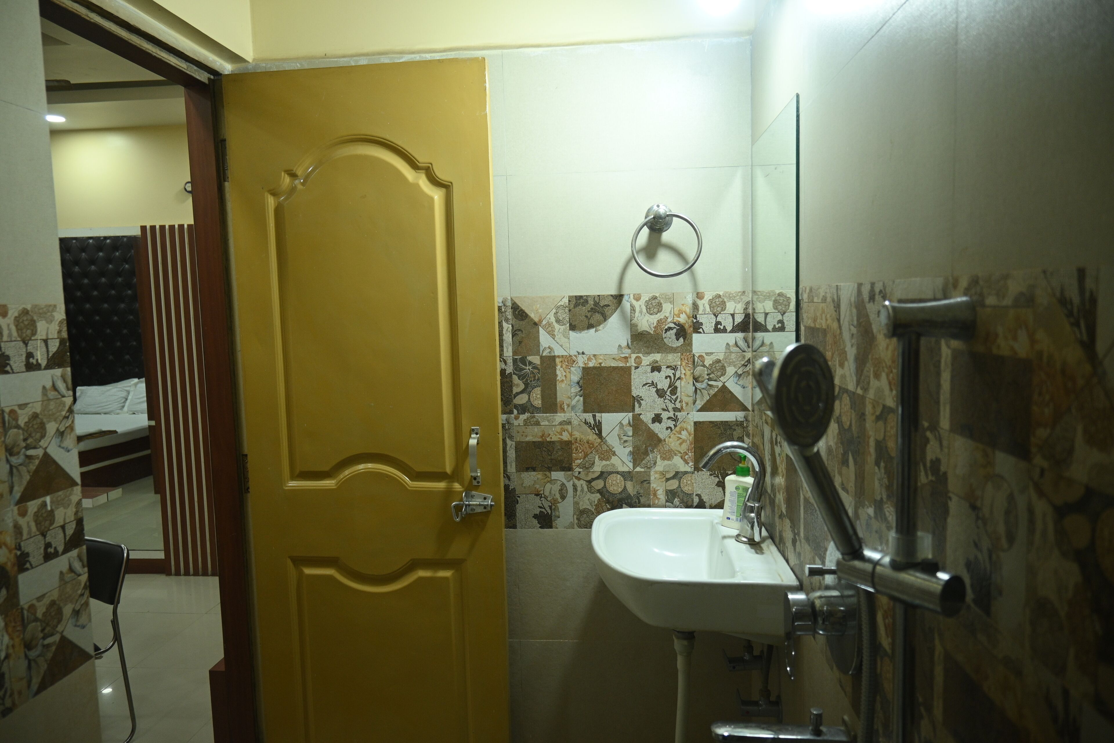 A bathroom with a yellow door, a sink with a mirror, and patterned tiles on the wall.
