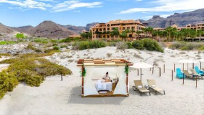 Un resort en el desierto con playa de arena, palmeras y un edificio grande al fondo.