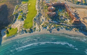 Luftaufnahme eines Küstenresorts mit Golfplatz, Strand und einem großen mehrstöckigen Hotelgebäude.