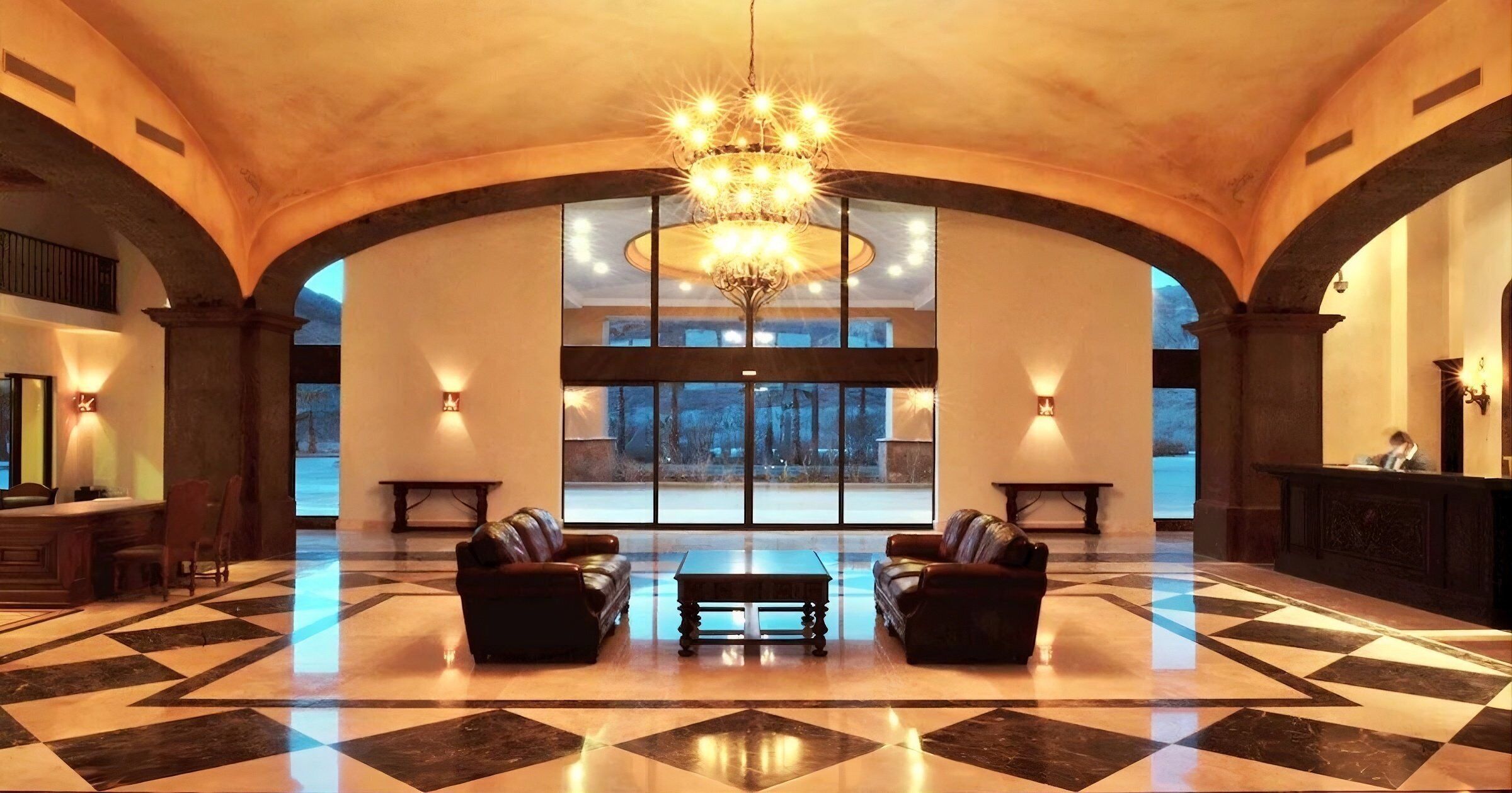 A spacious lobby with a high ceiling, a chandelier, leather sofas, a coffee table, and a reception desk.