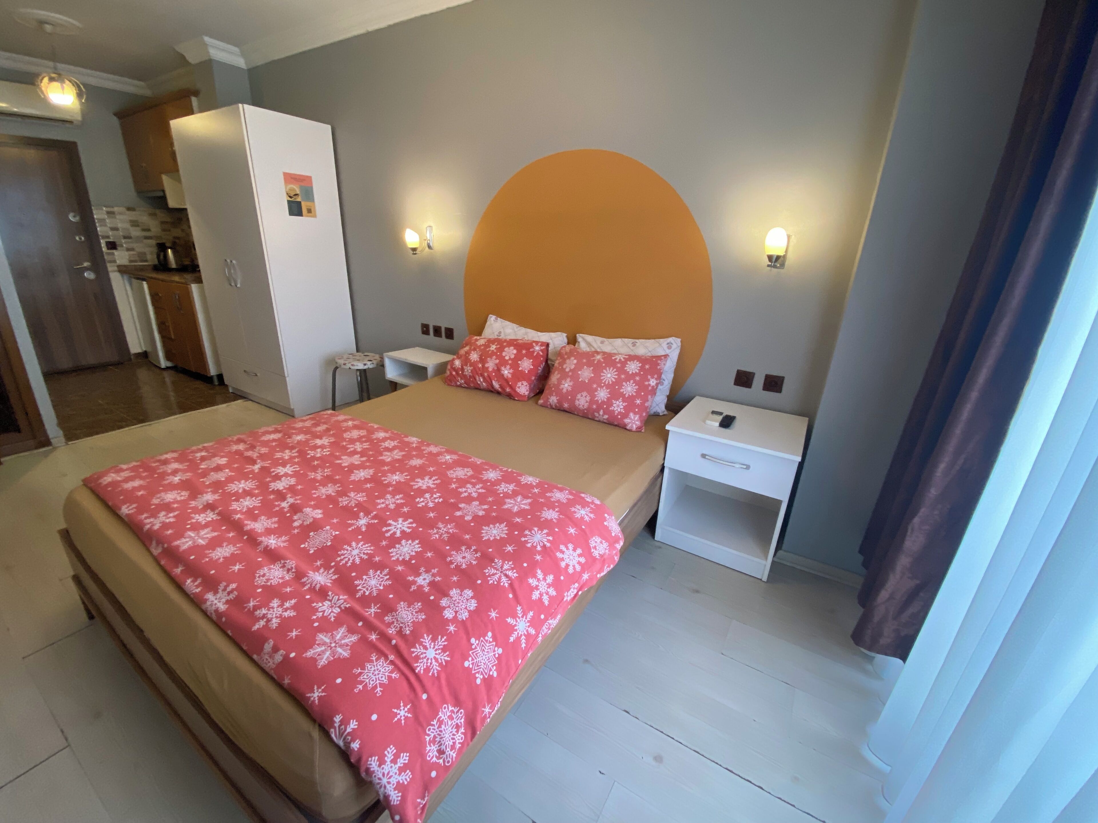 Un dormitorio con cama, mesitas de noche, cómoda y una zona de cocina al fondo.