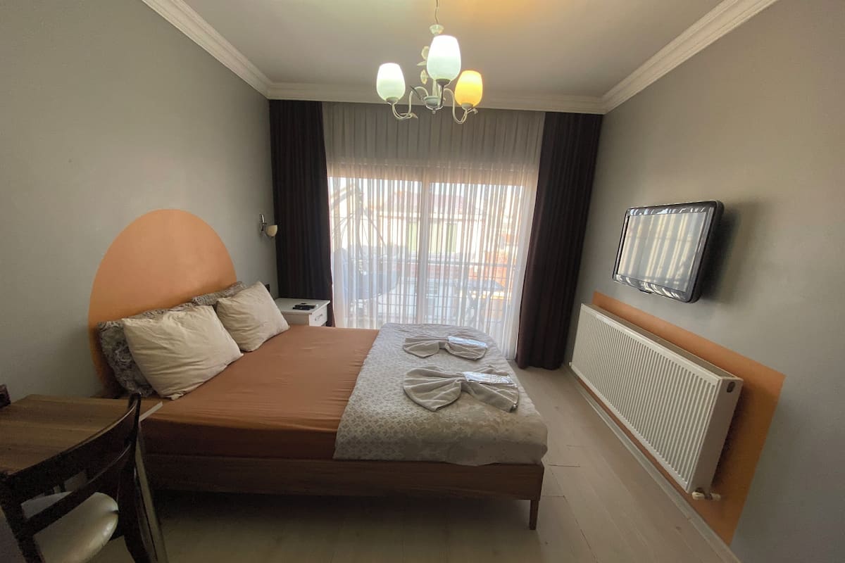 Habitación de hotel con cama, una silla, escritorio, televisor y ventana con cortinas.