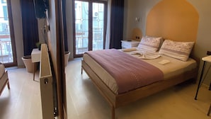 Et soveværelse med en stor seng, et natbord, en lampe, et tv ophængt på væggen og en skydedør, der fører ud til en balkon.