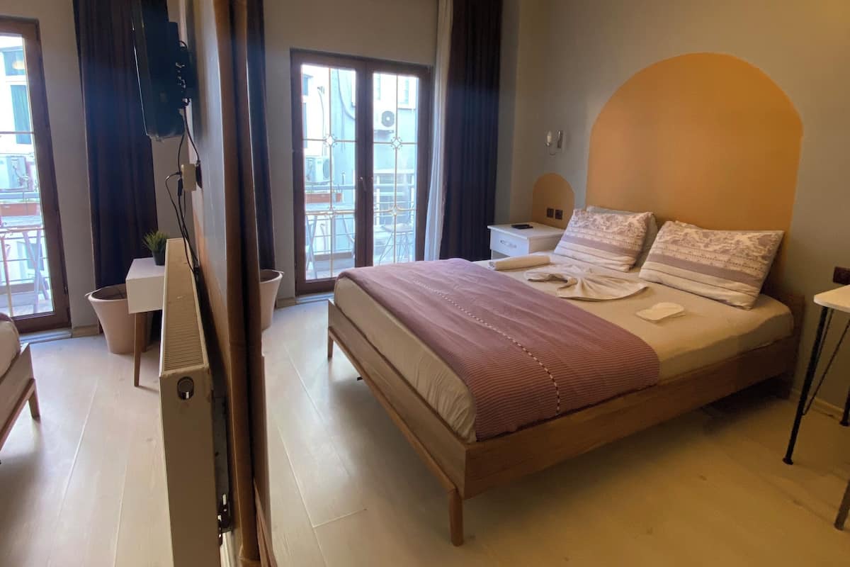 Un dormitorio con una cama grande, una mesita de noche, una lámpara, un televisor montado en la pared y una puerta corrediza que da a un balcón.