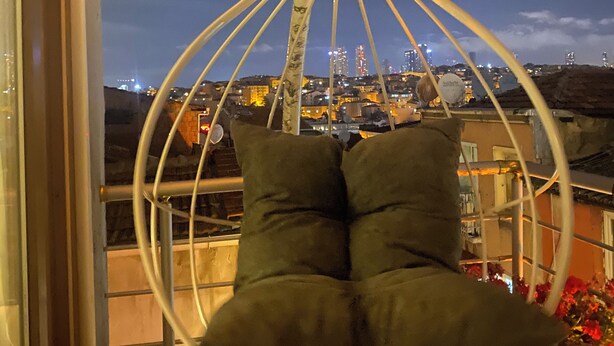 En hængestol med puder på en balkon med udsigt over bybilledet.