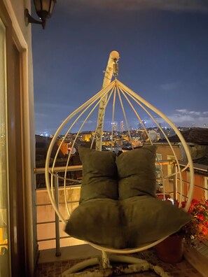 A hanging chair with cushions on a balcony with a cityscape view. - Omar Suite 360 (İstanbul)
