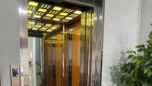 En elevator med metalindretning, en plante ved siden af og et mønstret gulv.