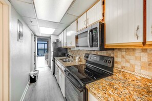 Eine schmale Küche mit weißen Schränken, einer Mikrowelle, einem Backofen und einer Arbeitsplatte aus Granit.