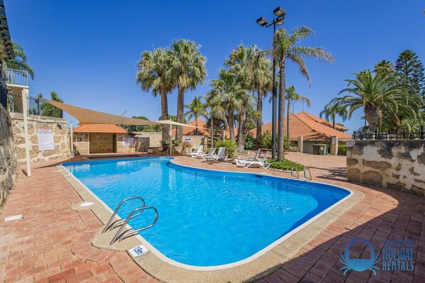 A swimming pool with lounge chairs, palm trees, and a stone wall. - Mandurah Family Splash (Mandurah)