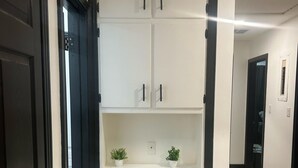 A hallway with a white wardrobe featuring black handles, a light switch, and two potted plants on the top shelf. - Bobby Rush Inn 3 bedroom 1.5 Bath modern house (Jackson)