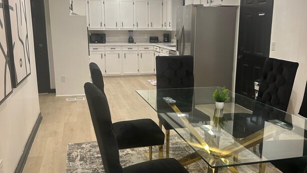A modern dining area with a glass table, black upholstered chairs, and a unique spherical light fixture. - Bobby Rush Inn 3 bedroom 1.5 Bath modern house (Jackson)