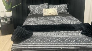 A bed with a patterned bedspread and pillows, a black throw blanket, and a black headboard. There is a small bedside table with a plant and a lamp. - Bobby Rush Inn 3 bedroom 1.5 Bath modern house (Jackson)