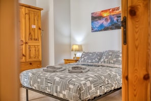 Een slaapkamer met een bed, een houten garderobe, een nachtkastje met een lamp en een schilderij aan de muur.
