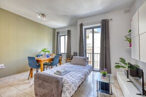 Un dormitorio moderno con cama, una mesa de comedor con sillas, televisor y balcón con cortinas.