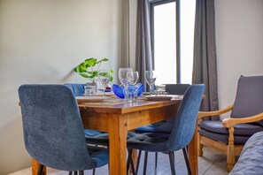 Een eetgedeelte met een houten tafel gedekt voor vier personen, blauwe bekleden stoelen en een plant op de tafel.