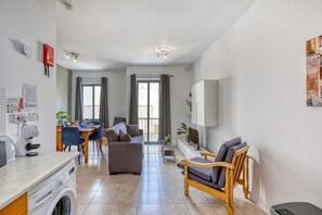 Een modern appartement met een keuken, een eethoek en een woonkamer. Er is een wasmachine, een eettafel met stoelen, een bank en een televisie.