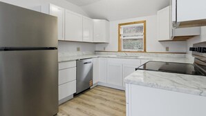 Een moderne keuken met witte kastjes, een roestvrijstalen koelkast, een vaatwasser en een raam met uitzicht.