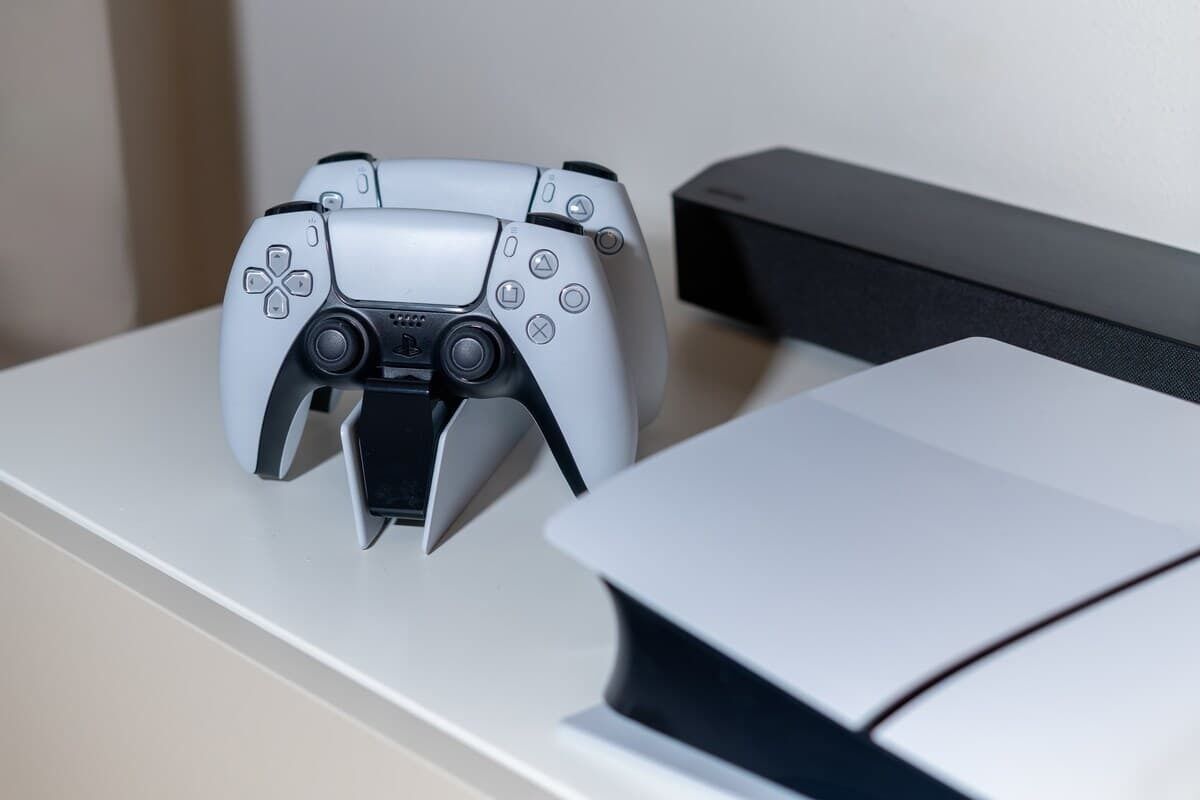 A PlayStation controller on a white surface next to a black PlayStation console.