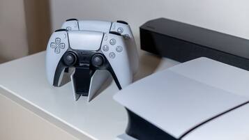 A PlayStation controller on a white surface next to a black PlayStation console.