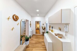 Un pasillo con suelo de madera, paredes blancas y un mostrador blanco con un teléfono y objetos decorativos.
