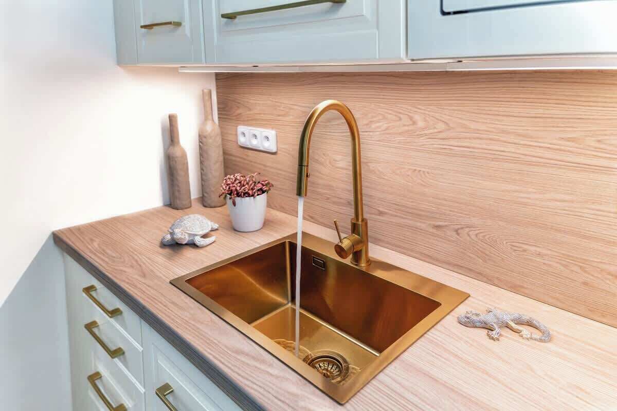 Una cucina con lavello in acciaio inossidabile, piano di lavoro in legno e mobili bianchi.