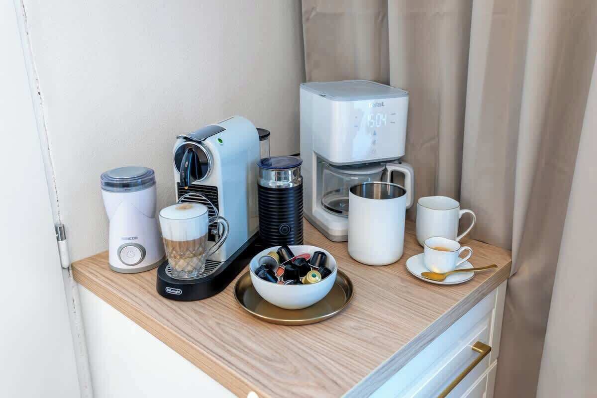 Una kitchenette con cafetera, licuadora, jarra de café, un tazón de cápsulas de café y una taza de café sobre una bandeja.