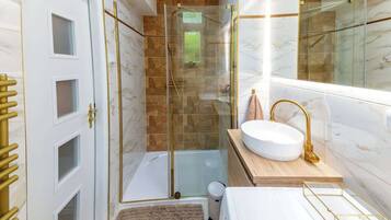 Ein modernes Badezimmer mit einer gläsernen Duschkabine, einem weißen Waschbecken mit goldfarbenen Armaturen und einem marmorbelagten Duschbereich.